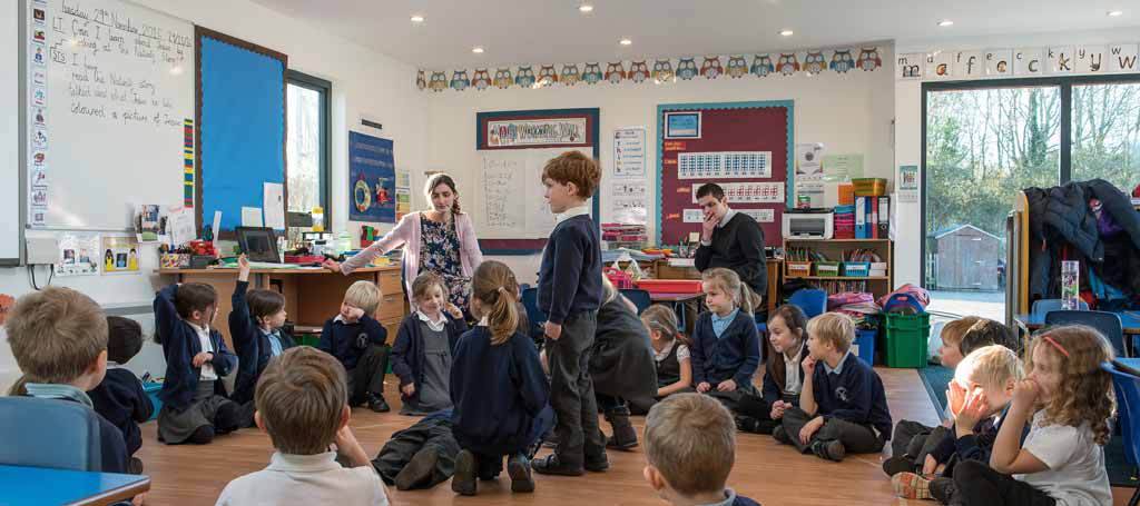 a primary school classroom with students sitting on the floor in a small space.